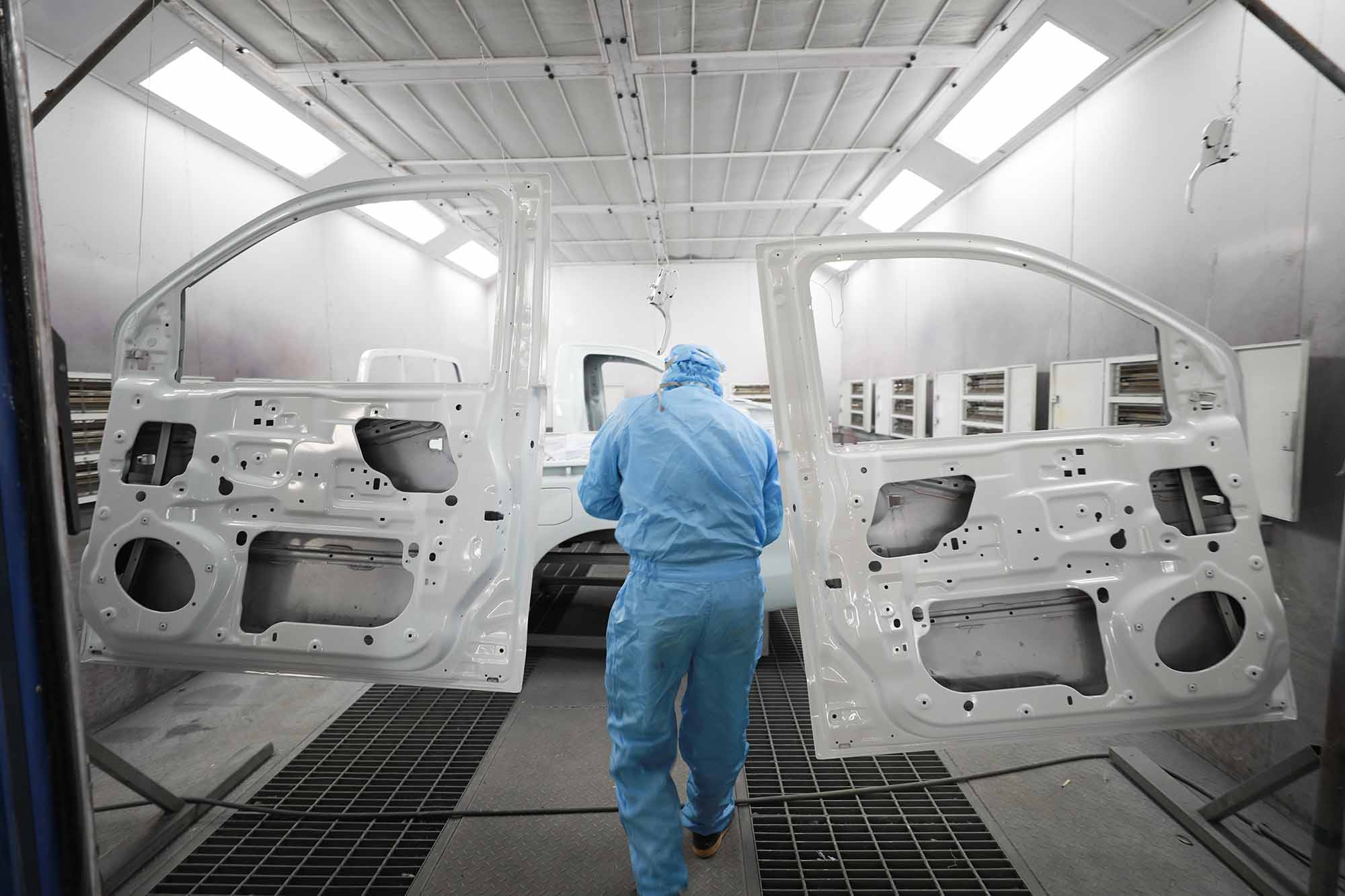 painter in blue protective suit between two white doors being painted - auto paint repair - browns collision center 