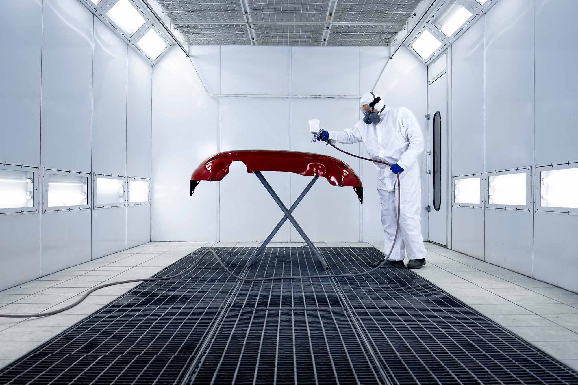 painter in white protective suit spraying red bumper in booth - auto paint repair - browns collision center